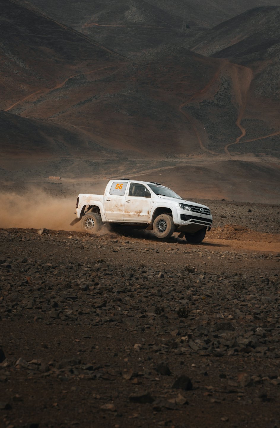 White pickup truck races across desert terrain kicking up dust.