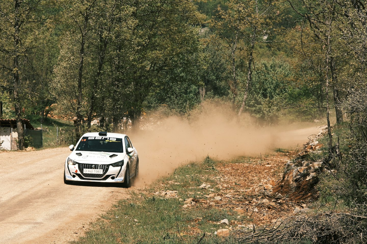 White rally car racing on a dirt track with dust.