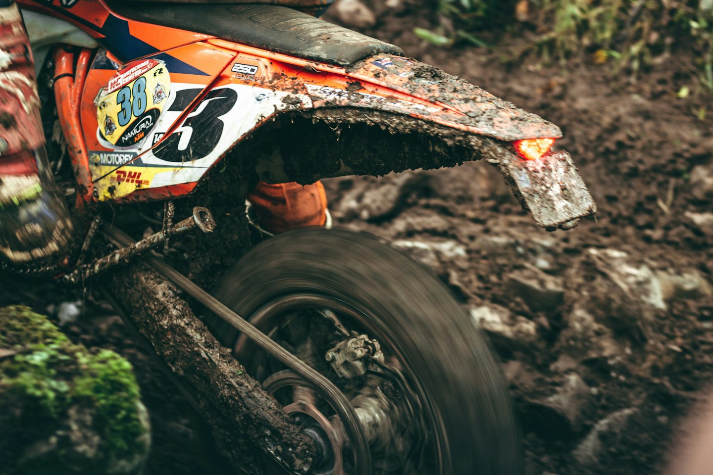 Orange dirt bike wheel kicking up mud on a trail.