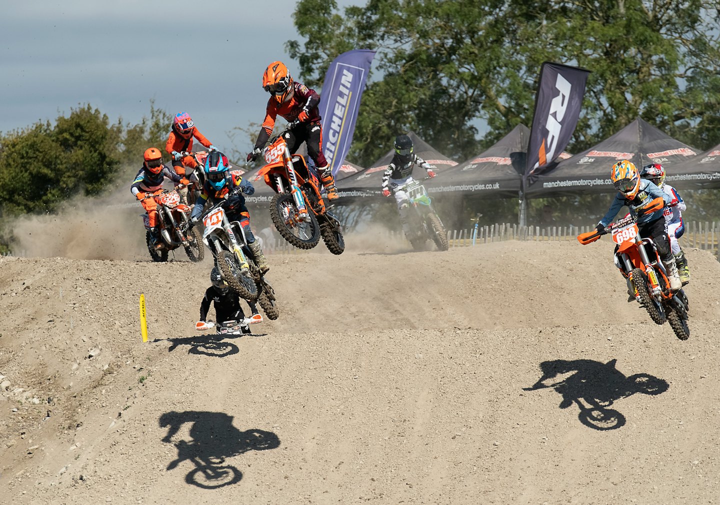 Motocross riders jump their dirt bikes over a large ramp.