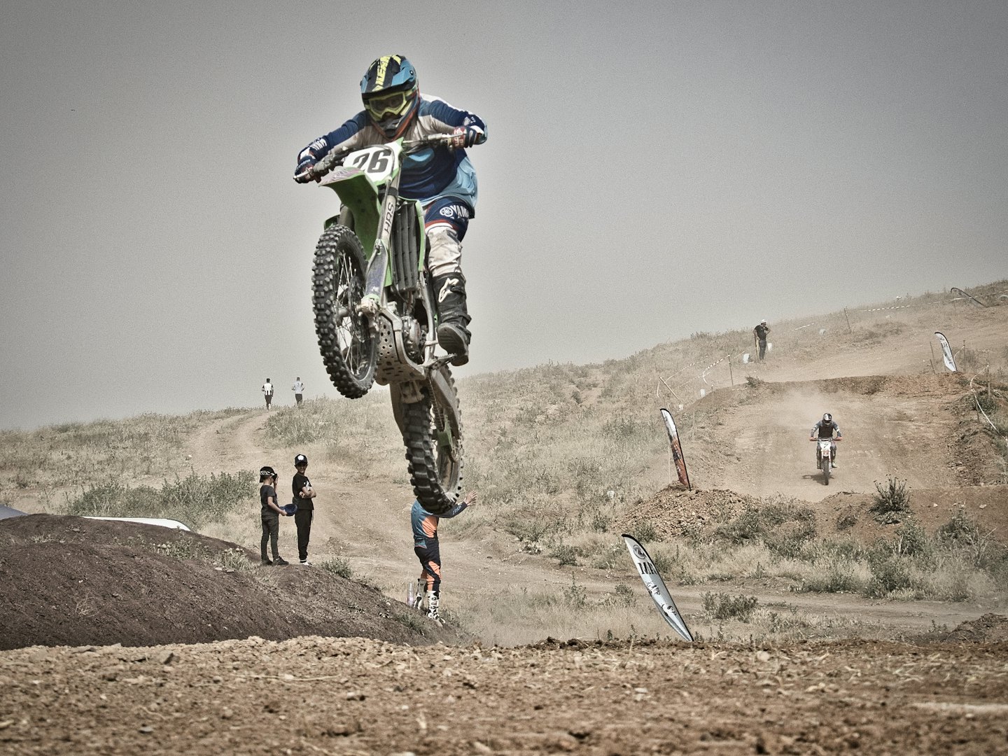 Motocross rider jumps a dirt mound on a green bike.