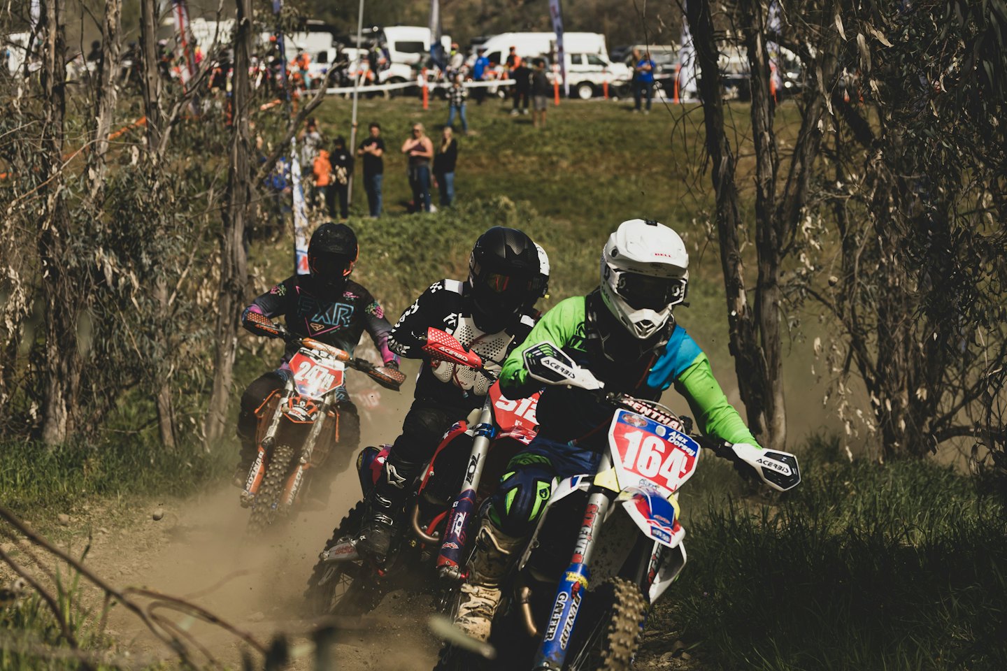 Three motocross riders race dirt bikes along a dusty track.