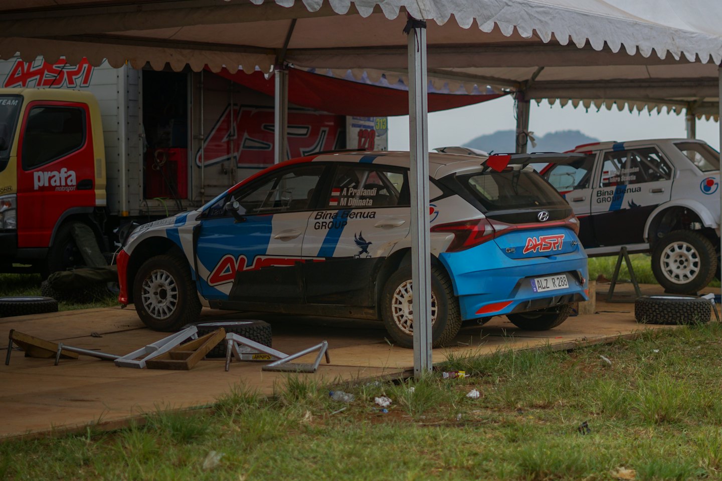 Two rally cars and a support truck sit under a tent.