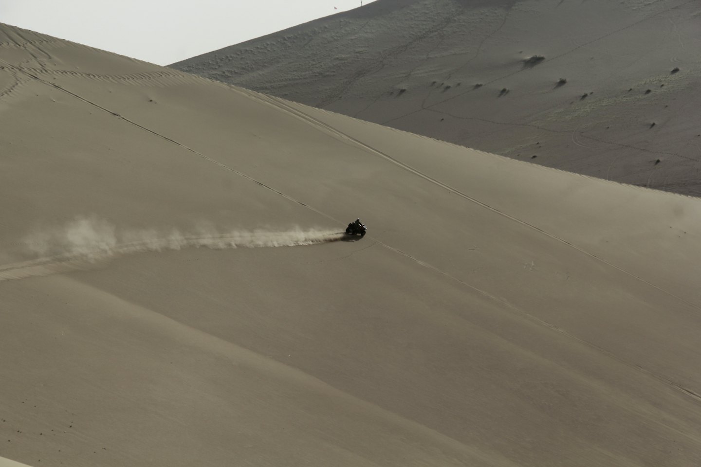 A person rides a quad bike down a sandy desert dune.