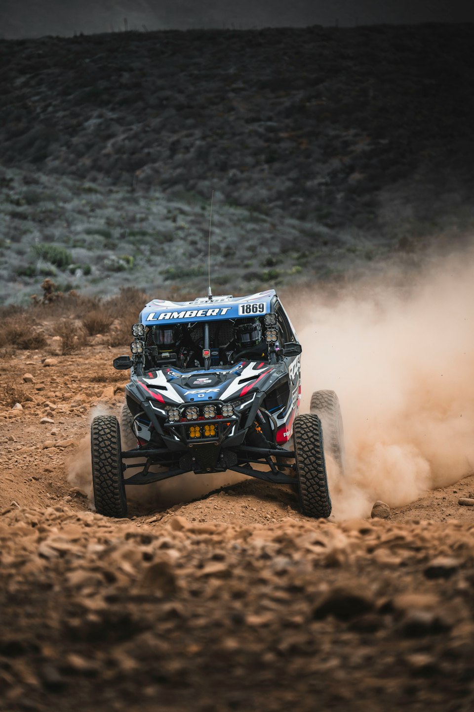 A utility vehicle races across a dusty rocky dirt track.