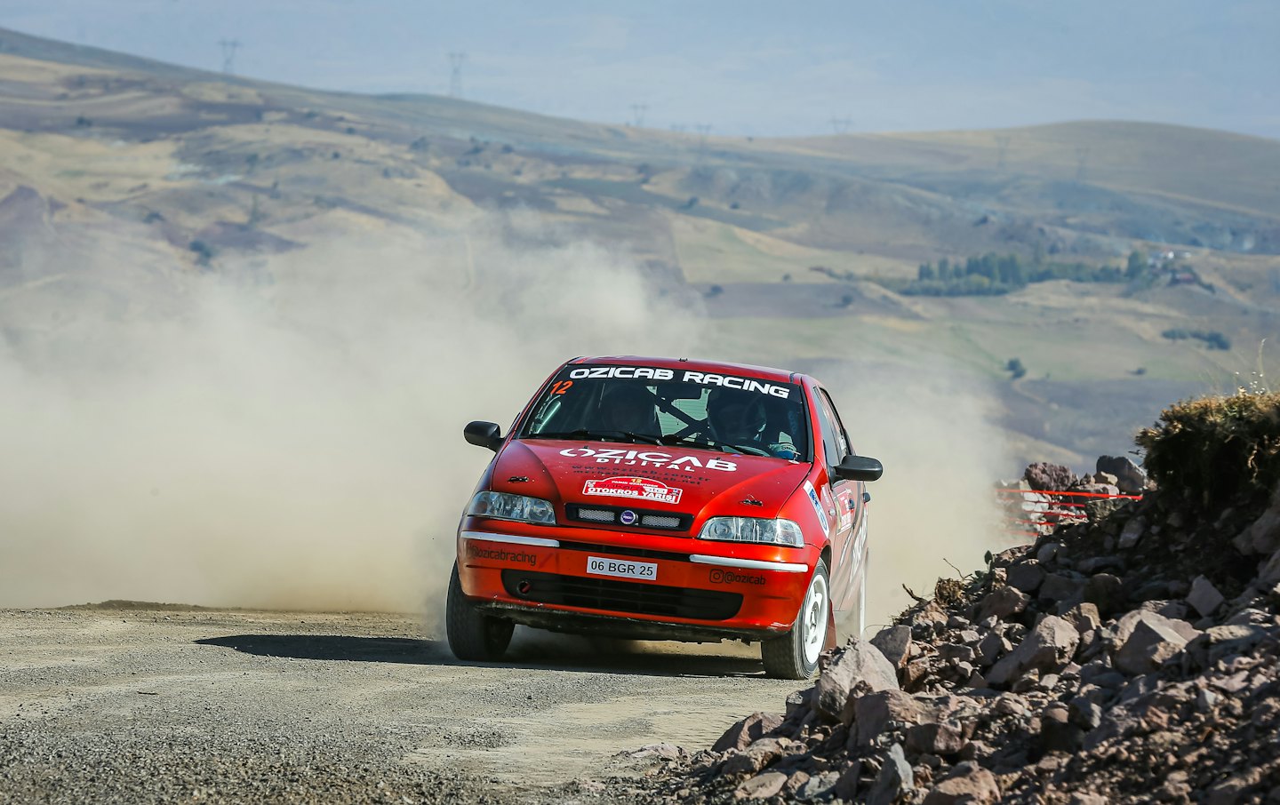A red rally car speeds along a dusty gravel road.