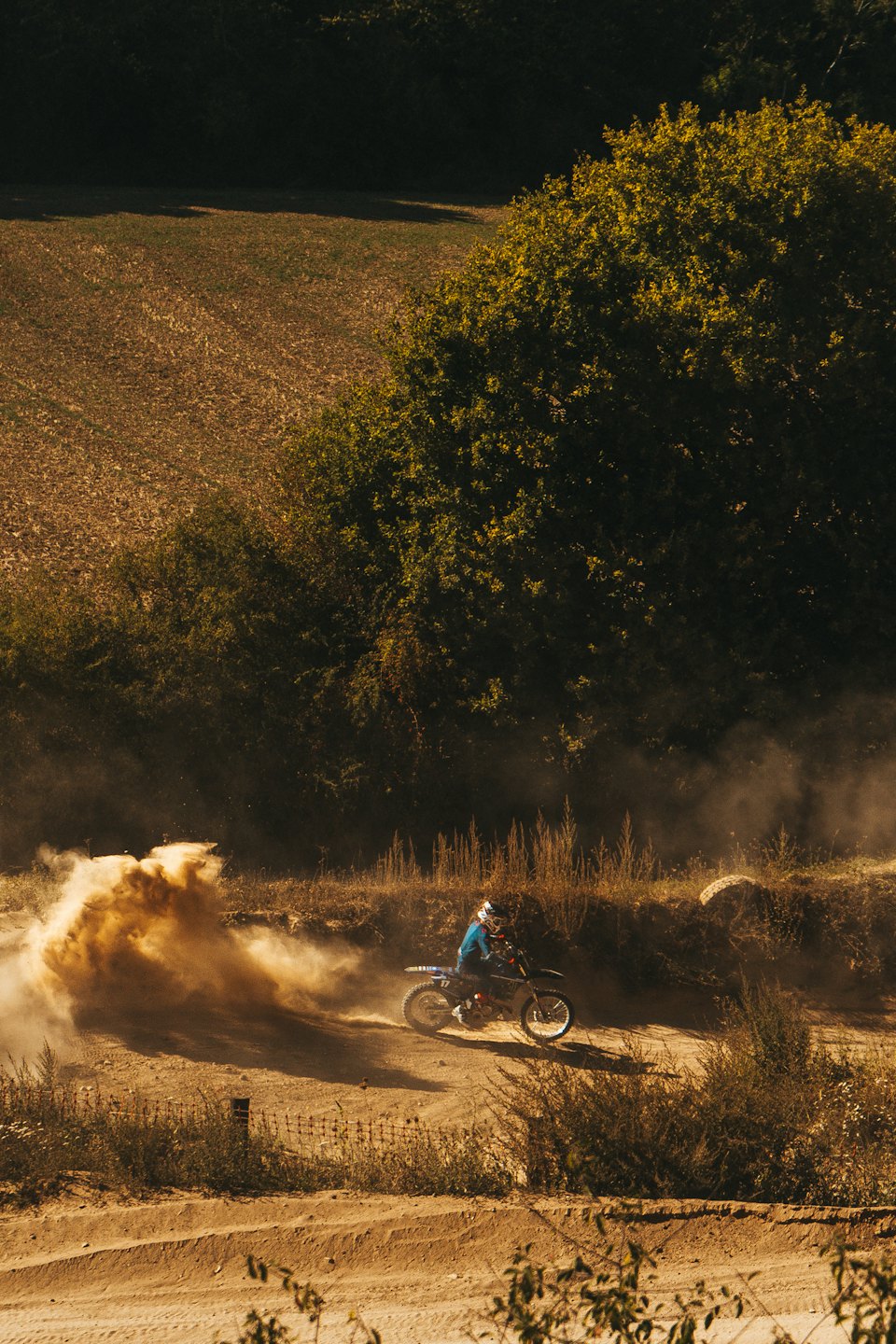 Rider in blue gear speeds along a dusty dirt track.